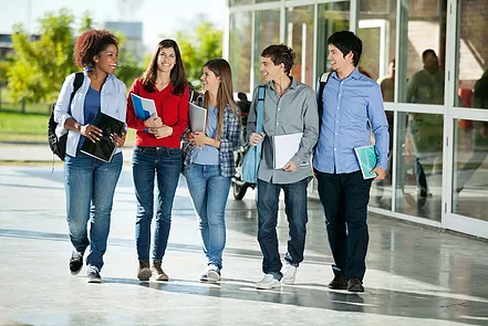 5 students walking on the outside of a glass building